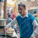 A street vendor prepares food in a bustling Varanasi alley, capturing local culture and daily life.